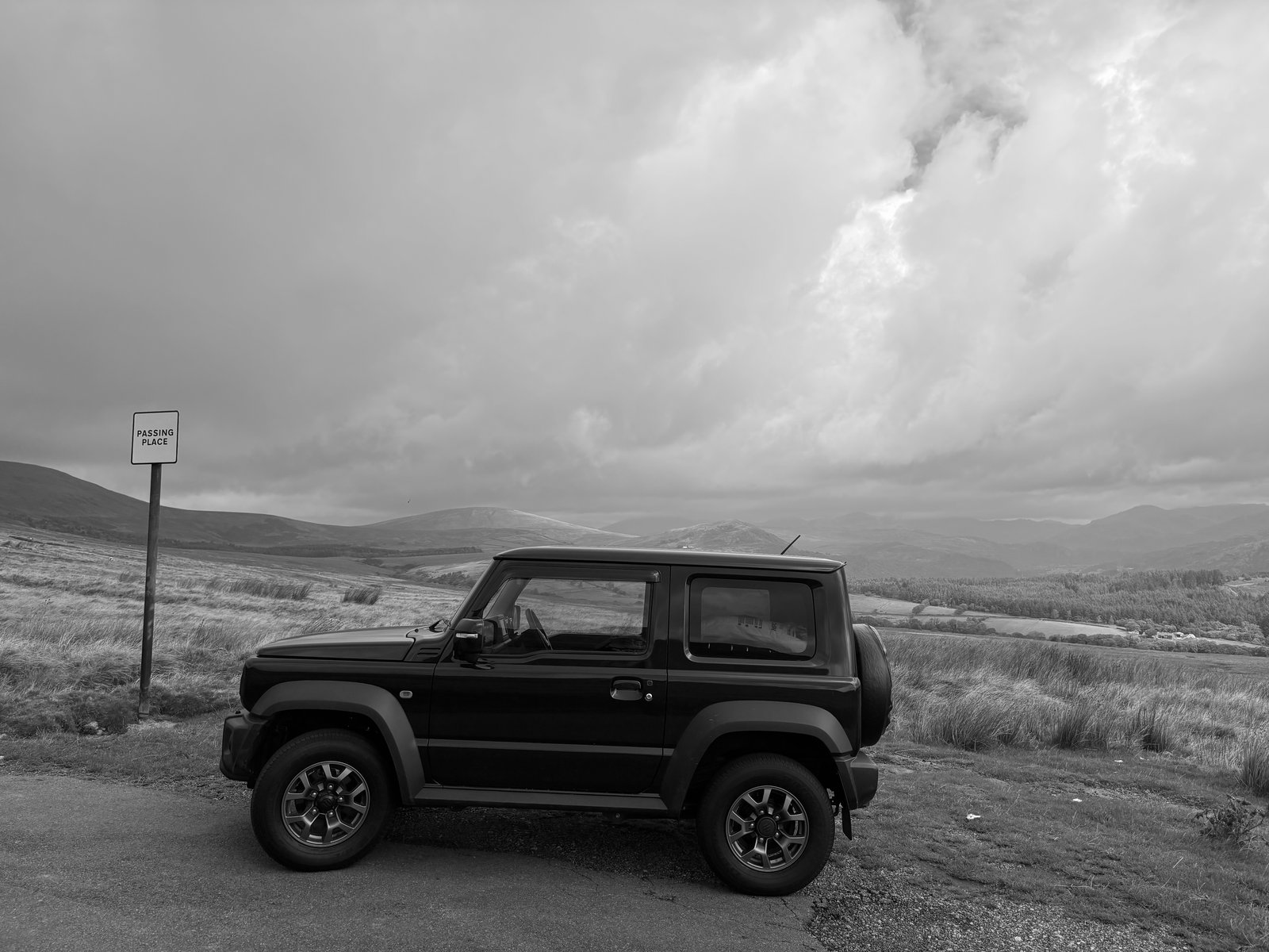 Jimny side profile beside a passing place sign on a hill road
